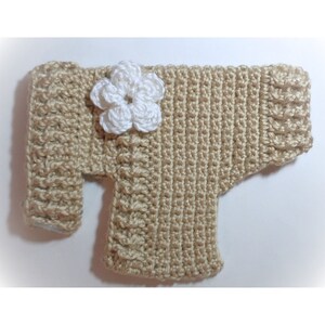 May include: A beige crocheted sweater for a small dog or cat, with a white crocheted flower embellishment.