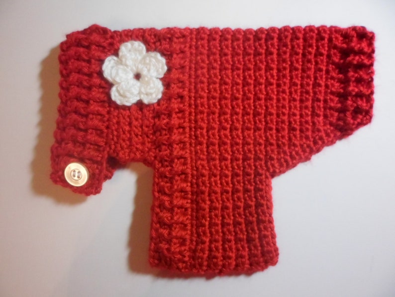 May include: Red crocheted sweater with a white crocheted flower and a button on the sleeve.