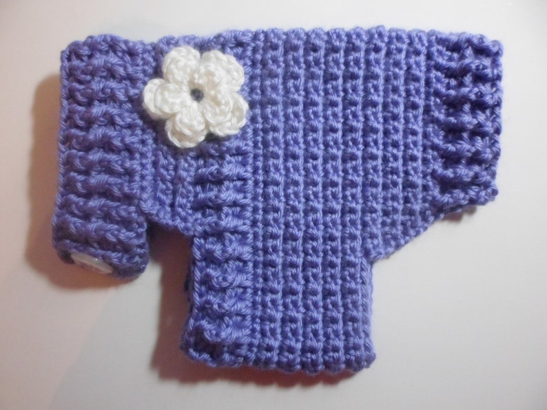 May include: A purple crocheted sweater with a white crocheted flower on the front.
