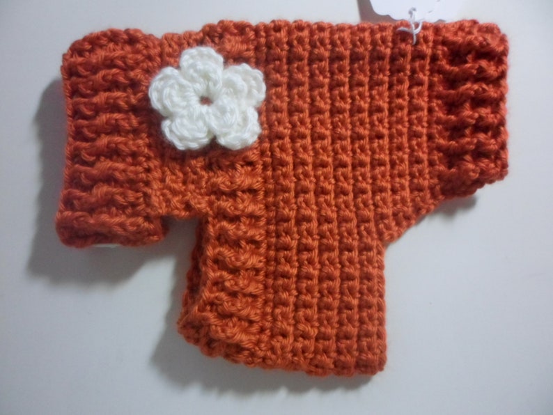 May include: A crocheted orange sweater with a white crocheted flower on the front.