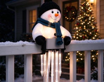 May include: A light-up snowman decoration wearing a black knit hat, a teal scarf, and black mittens. The snowman is mounted on a white railing and features a set of five hanging, illuminated clear icicle lights that glow with a warm white light.