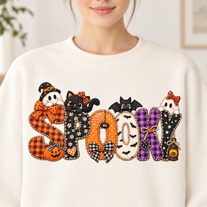 Puede incluir: Una sudadera de cuello redondo color crema con la palabra SPOOKY en letras grandes estampadas. El diseño incluye un fantasma con sombrero, un gato negro, un murciélago y una pequeña linterna, decorados con cuadros y lunares naranjas, negros y morados.