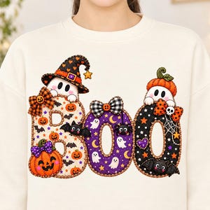 May include: A cream-colored crewneck sweatshirt featuring a large graphic of the word BOO. The letters are decorated with Halloween motifs including ghosts, orange pumpkins, black bats, purple stars, and plaid bows in orange and black.