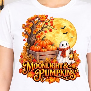 May include: A white short-sleeved t-shirt featuring a graphic of a ghost wearing a scarf and holding a lantern next to a wooden crate of pumpkins under a full moon and autumn tree. The text Moonlight & Pumpkins is printed in orange below.