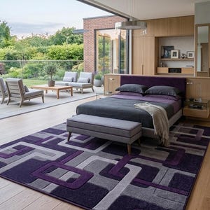 Peut inclure: Un tapis rectangulaire présentant un motif géométrique de carrés et de rectangles entrelacés dans des tons de violet profond, de gris clair et de gris anthracite. Le tapis a une texture à poils ras et repose sur un parquet en bois clair.