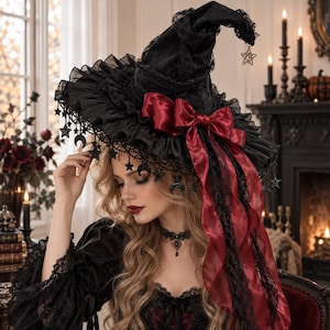 May include: A black lace witch hat featuring a deep red satin bow, ruffled trim, and dangling metal star and crescent moon charms. The hat has a pointed crown and a wide brim adorned with intricate black lace detailing and hanging ornaments.