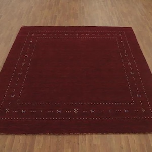May include: A square area rug in a deep solid red color featuring a decorative border. The border consists of a series of small white dots arranged in a rectangular frame, interspersed with tiny stylized animal and floral motifs in light colors.