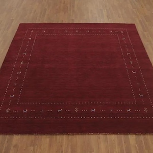 May include: A rectangular area rug in a deep burgundy red color featuring a central solid field surrounded by a decorative border. The border is composed of small white dotted lines interspersed with tiny, stylized animal and plant motifs.
