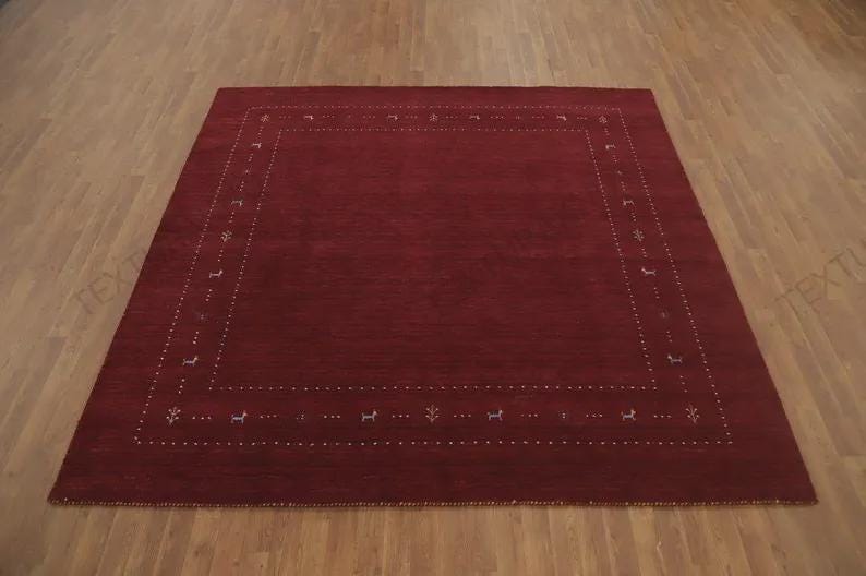 May include: A rectangular area rug in a deep burgundy red color featuring a central solid field surrounded by a decorative border. The border is composed of small white dotted lines interspersed with tiny, stylized animal and plant motifs.