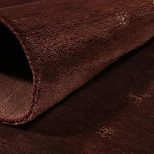 May include: A deep brown rug with a soft, dense pile texture, partially folded over to reveal the underside. The surface features a subtle, repeating pattern of small, light-colored, stylized animal figures scattered across the dark fabric.
