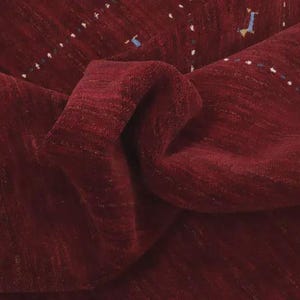 May include: A deep burgundy rug with a textured, pile surface. The rug features subtle, horizontal rows of small, embroidered accents in white, blue, and yellow, creating a delicate pattern across the rich, dark red fabric of the floor covering.