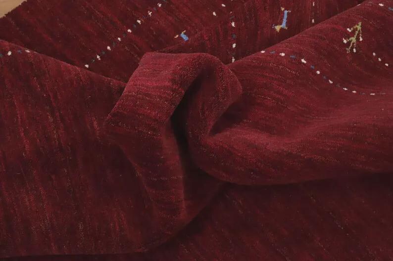 May include: A deep burgundy rug with a textured, pile surface. The rug features subtle, horizontal rows of small, embroidered accents in white, blue, and yellow, creating a delicate pattern across the rich, dark red fabric of the floor covering.