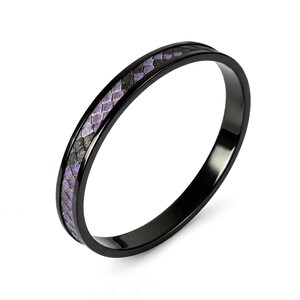 May include: A thin black ring featuring a central inlay with a textured, scale-like pattern in alternating shades of purple and dark gray. The band has a smooth, polished finish and a rounded profile, showcasing a distinct contrast between the dark metal.
