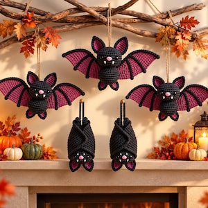 May include: Five crocheted bat ornaments featuring black bodies and purple wing accents. Three bats are displayed with wings spread wide, while two bats are shown hanging in a folded position. Each bat has small white fangs and a pink nose.