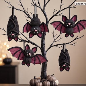 May include: Five handmade crochet bat ornaments in black and dark purple yarn, hanging from a black decorative tree. The bats feature small pink noses and white fangs. The text ShahCrochetNest is visible in the top right corner of the image.