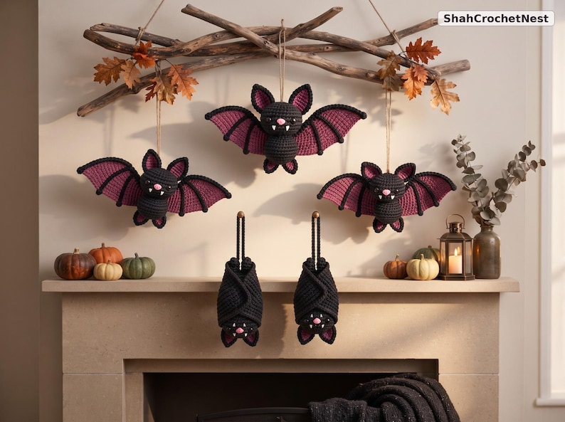 May include: Three crocheted bats with black bodies and purple wing accents hanging from a wooden branch, and two additional crocheted bats hanging vertically below. The bats feature small white fangs and pink noses. Text reads ShahCrochetNest.