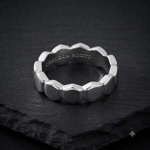 Könnte beinhalten: Ein silberfarbener Ring mit einem sich wiederholenden sechseckigen Muster um das Band. Die Innenseite des Rings ist mit dem Text Kendra Scott graviert. Die Metalloberfläche hat ein poliertes Finish, das an den Kanten reflektiert.