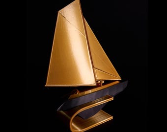 Op de afbeelding: Een decoratief zeilbootbeeld met een metallic gouden zeil en een donkerzwarte romp. Het schip is gemonteerd op een gebogen, goudkleurige voet die zorgt voor een strakke, verhoogde uitstraling. Het ontwerp benadrukt scherpe geometrische lijnen.