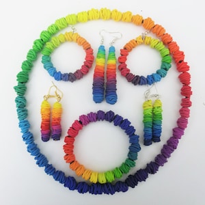 May include: A rainbow-colored necklace, bracelet, and earrings set made of polymer clay. The set features a variety of rainbow colors, including red, orange, yellow, green, blue, indigo, and violet.