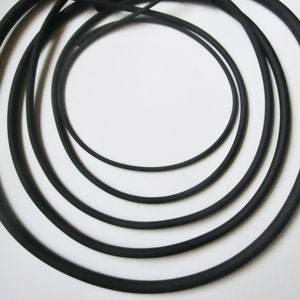 May include: Five black rubber bands of different sizes, arranged in a concentric circle pattern.