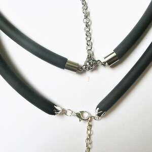 May include: A black rubber necklace with a silver chain and clasp. The necklace is made of two layers of rubber.