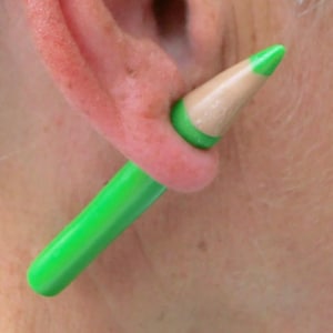 May include: A green and beige pencil-shaped earring with a green tip.
