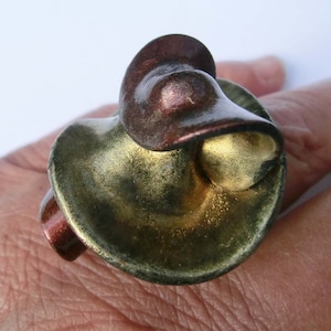 Puede incluir: Un anillo de oro y cobre con un diseño abstracto único. El anillo está hecho de metal y tiene una superficie texturizada.