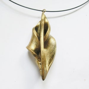 May include: A gold-colored pendant necklace with a unique, abstract design. The pendant is made of a smooth, metallic material and has a twisted, organic shape.
