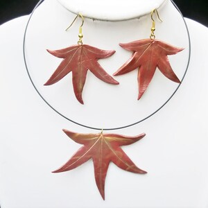 May include: A set of red and gold leaf earrings and necklace. The leaves are made of polymer clay and have a realistic look. The necklace is a simple black cord with a single leaf pendant.
