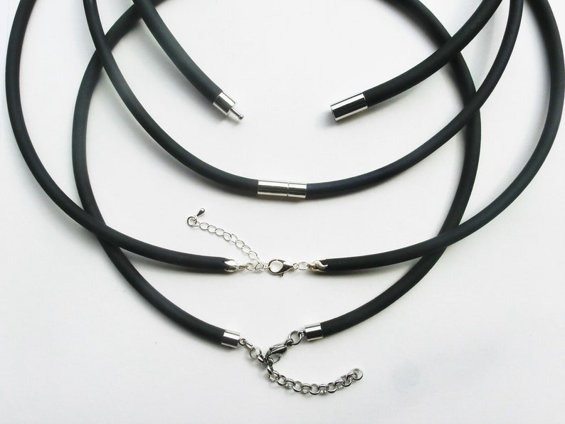 May include: Three black elastic cord necklaces with silver metal clasps and connectors. The necklaces are layered on top of each other.