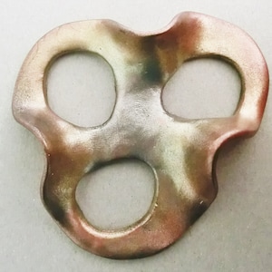 Könnte beinhalten: Eine abstrakte Keramikskulptur in Metallic-Gold, Grün und Braun mit drei Löchern. Die Skulptur hat eine wellenförmige, organische Form.