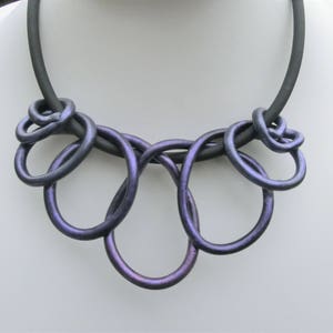 May include: A black choker necklace with a purple iridescent multi-loop design. The necklace is made of polymer clay and is a statement piece.