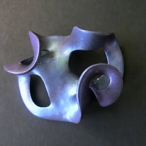 Op de afbeelding: Een blauwe en paarse keramische sculptuur met een abstracte, organische vorm. De sculptuur heeft verschillende gaten en bochten, waardoor een gevoel van beweging en stroming ontstaat.