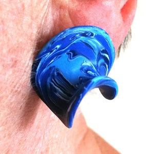 May include: A blue and white marbled ear gauge with a curved shape.