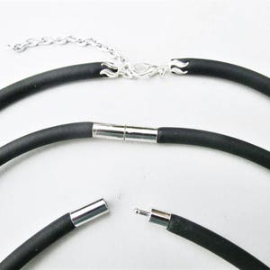 May include: A black rubber necklace with a silver clasp and a magnetic closure. The necklace is shown in three different positions, with the clasp and closure visible.