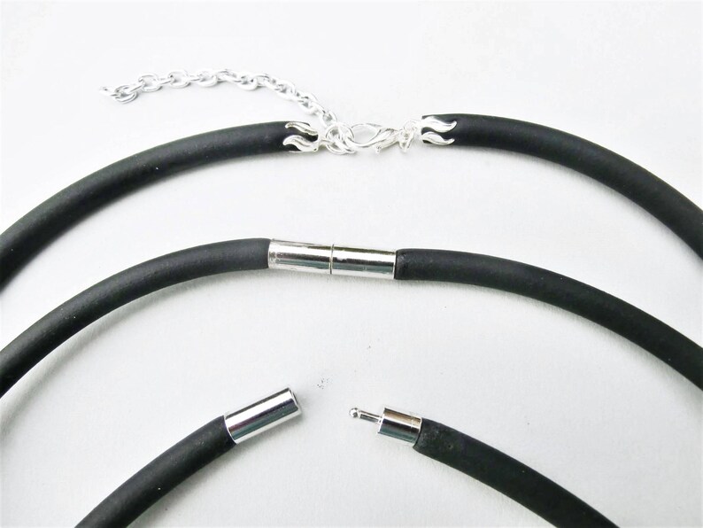 May include: A black rubber necklace with a silver clasp and a magnetic closure. The necklace is shown in three different positions, with the clasp and closure visible.