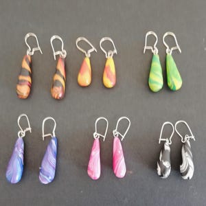 May include: A set of ten handmade dangle earrings with a variety of colourful patterns. The earrings are made of polymer clay and have silver hooks.