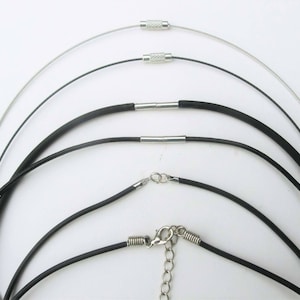 Könnte beinhalten: Ein Set aus fünf Halsketten, darunter eine silberne Kette und vier schwarze Gummibänder. Die Halsketten sind alle unterschiedlich lang und haben silberne Verschlüsse.