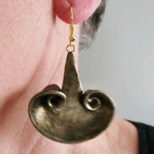 May include: A pair of gold-tone earrings with a unique, abstract design. The earrings feature a swirling, organic shape with a pointed top.