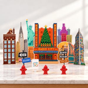 May include: A decorative New York City skyline set featuring cutouts of the Radio City Music Hall, the Statue of Liberty, and various skyscrapers. Includes three red fire hydrants, street signs labelled One Way, Broadway, and New York.