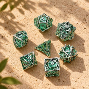 Puede incluir: Un juego de siete dados poliédricos con un diseño de jaula de metal plateado, intrincados motivos de hojas y detalles en esmalte verde vibrante. Cada dado muestra números claros en relieve, destacando un tema botánico detallado.