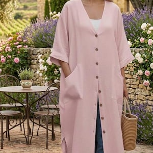Peut inclure: Un long gilet rose clair de type duster avec une encolure en V, une fermeture boutonnée sur toute la longueur avec des boutons marron, des manches larges arrivant aux coudes et deux grandes poches plaquées sur le devant. Fentes latérales.