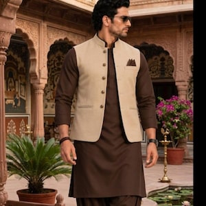 May include: A dark brown long-sleeved kurta paired with matching loose-fitting trousers and a beige sleeveless Nehru jacket. The jacket features a mandarin collar, a row of five buttons, two side pockets, and a small brown pocket square.