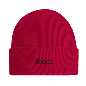 Könnte beinhalten: Eine leuchtend rote, gerippte Strickmütze mit umgeschlagenem Saum. Das Wort "Blocc" ist in schwarzem Garn mittig auf den Saum gestickt. Die Mütze hat eine abgerundete Krone und ein strukturiertes, vertikales Rippenmuster im gesamten Stoff.