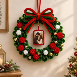 May include: A green pipe cleaner Christmas wreath featuring a large red and green bow at the top, red and white pom-poms, and gold spheres. A rectangular frame hangs from the center, displaying a photograph of a couple embracing.