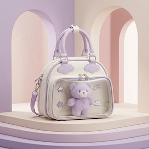 May include: A cream-coloured handbag with lavender accents, featuring a clear front pocket containing a plush lavender teddy bear and small star and cloud-shaped pins. The bag has two top handles and a detachable shoulder strap.