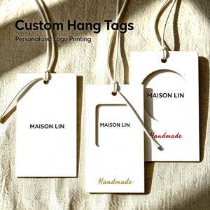 May include: Three rectangular white hang tags with white strings. The tags feature the black text MAISON LIN, with one tag showing a rectangular cutout and the word Handmade in gold, and another showing a circular cutout and the word Handmade in red.