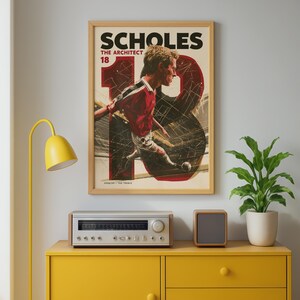 May include: A framed poster featuring a soccer player in a red and white uniform, with the text SCHOLES THE ARCHITECT 18 and 1998/99 THE TREBLE. The artwork displays a large number 18 in the background with dynamic lines and a soccer ball.