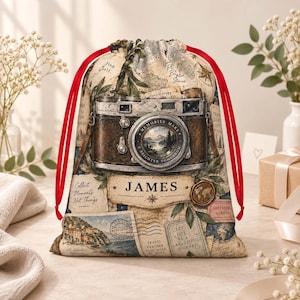 May include: A drawstring bag featuring a vintage camera illustration, a map background, and the name JAMES printed on a central label. The bag has bright red cords and includes text such as Memories Make A Brighter Tomorrow and Collect Moments Not Things.