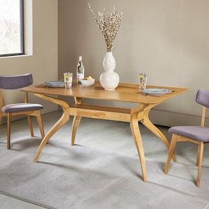 May include: A light oak dining table with a central shelf and curved legs, accompanied by two chairs with grey upholstered seats. On the table are two clear glasses, a white bowl, a glass bottle, and a white vase containing pussy willow branches.